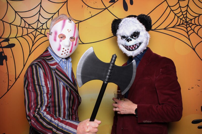 two men in masks wearing halloween costumes in front of a halloween backdground party photo booth